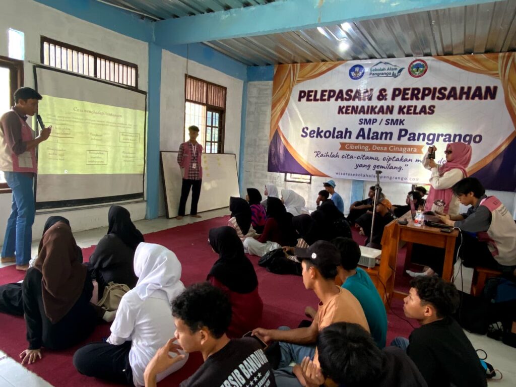 Dua mahasiswa FESEB UIC sedang mempresentasikan materi menggunakan proyektor di depan puluhan siswa yang duduk melantai di dalam ruangan kelas Sekolah Alam Pangrango, Desa Cinagara.